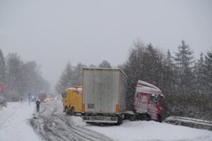 A truck accident on the road during severe winter conditions, requiring roadside assistance to manage the situation.