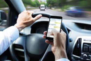 Close-up of a man's hand texting on a mobile phone while driving.