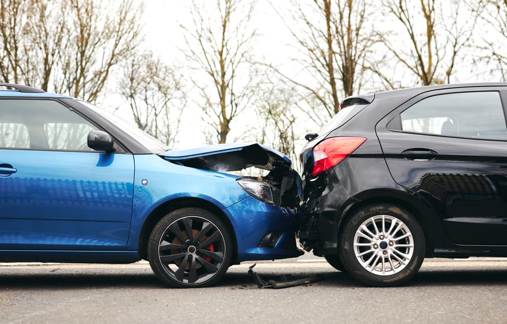 Two cars are involved in a traffic accident on the side of the road, showing damage to the hood and fender.