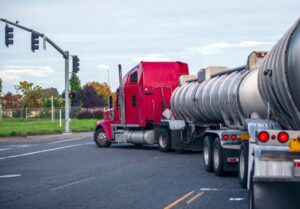 A big rig long-haul semi-truck with a two-tank semi-trailer navigates a traffic light intersection, transporting liquid and liquefied cargo.