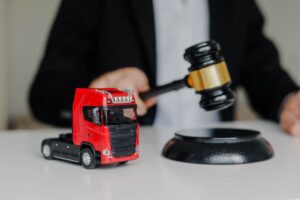 A male judge strikes a gavel on a block in the courtroom, symbolizing a prohibited export ruling. A toy cargo truck sits on the table, representing the export restriction concept.