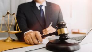 A lawyer reviewing contract documents at a desk in an office, with a brass scale symbolizing justice and the law.