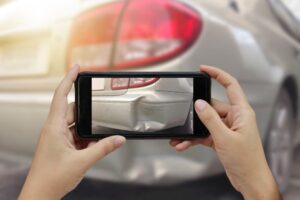 Close-up of a hand holding a smartphone, capturing a photo at the scene of a car crash for an insurance claim after the accident.